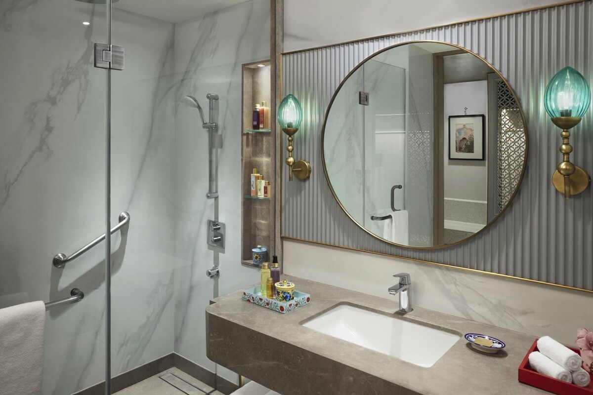Une salle de bain moderne avec une douche à parois de verre, un meuble-lavabo en marbre, un grand miroir rond et des appliques murales.