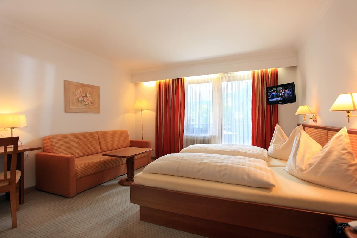 A hotel room with a bed, a sofa, a TV, and a desk.