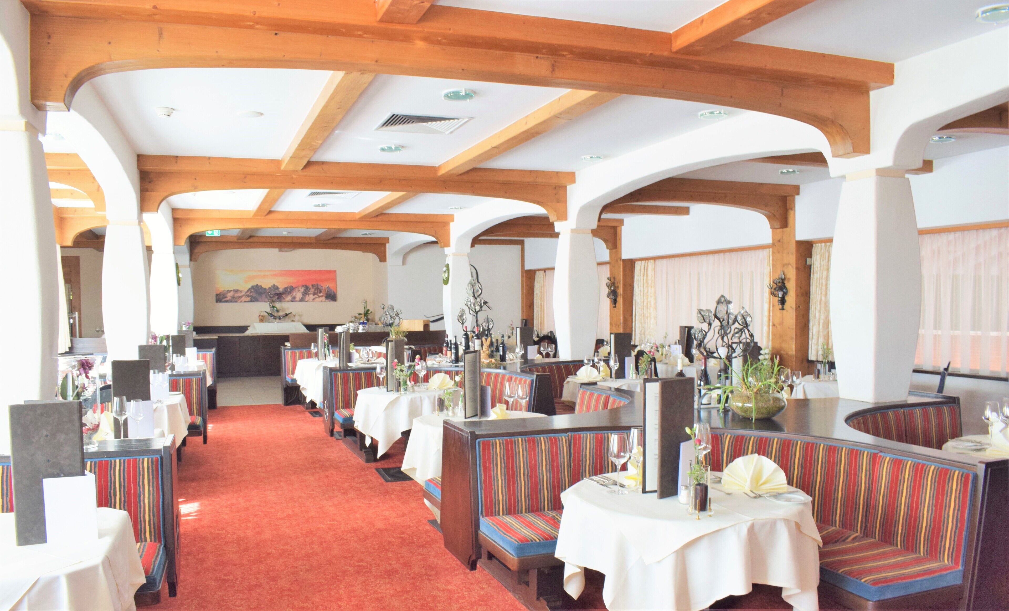 A restaurant with booths and tables, wooden beams on the ceiling, and a red carpet.