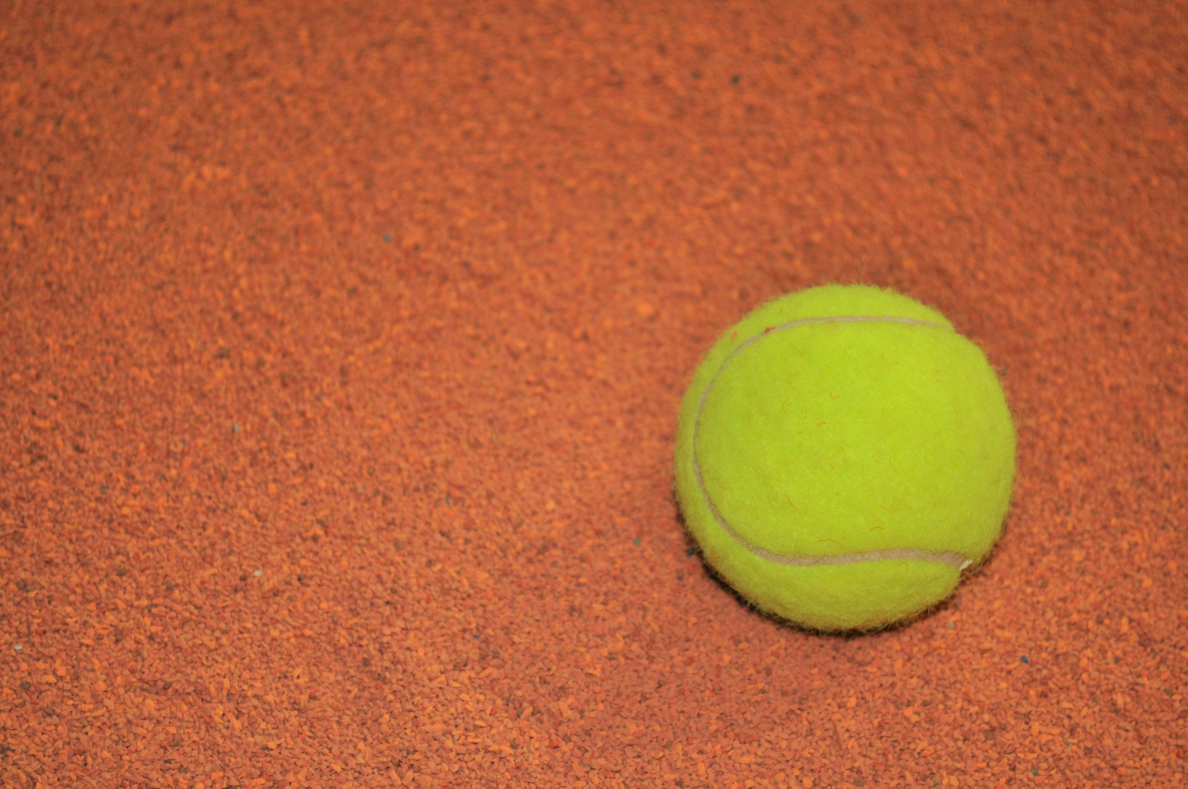 A tennis ball on a textured orange surface.
