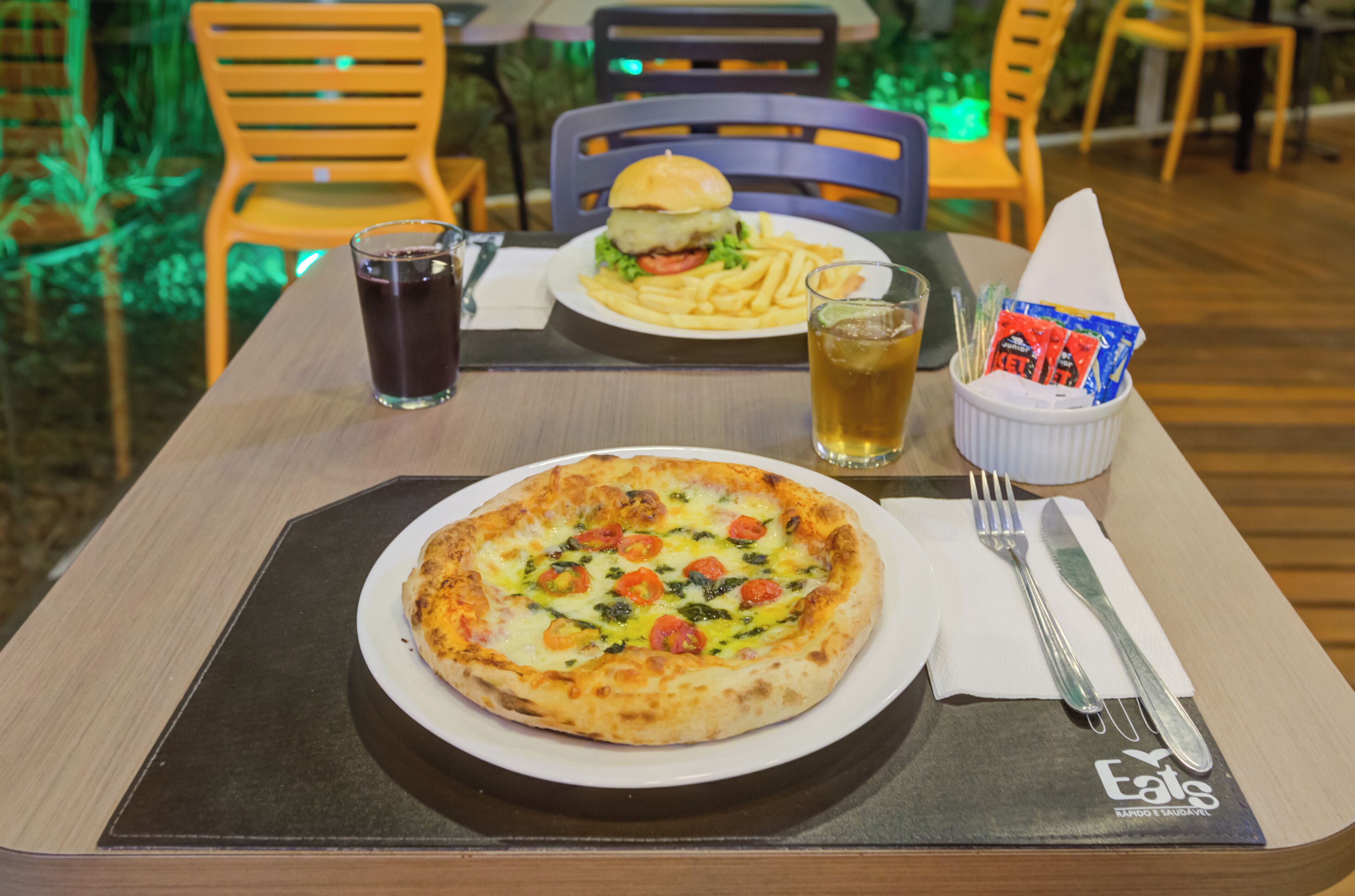 A dining table with a pizza, a burger, fries, a drink, and condiments.