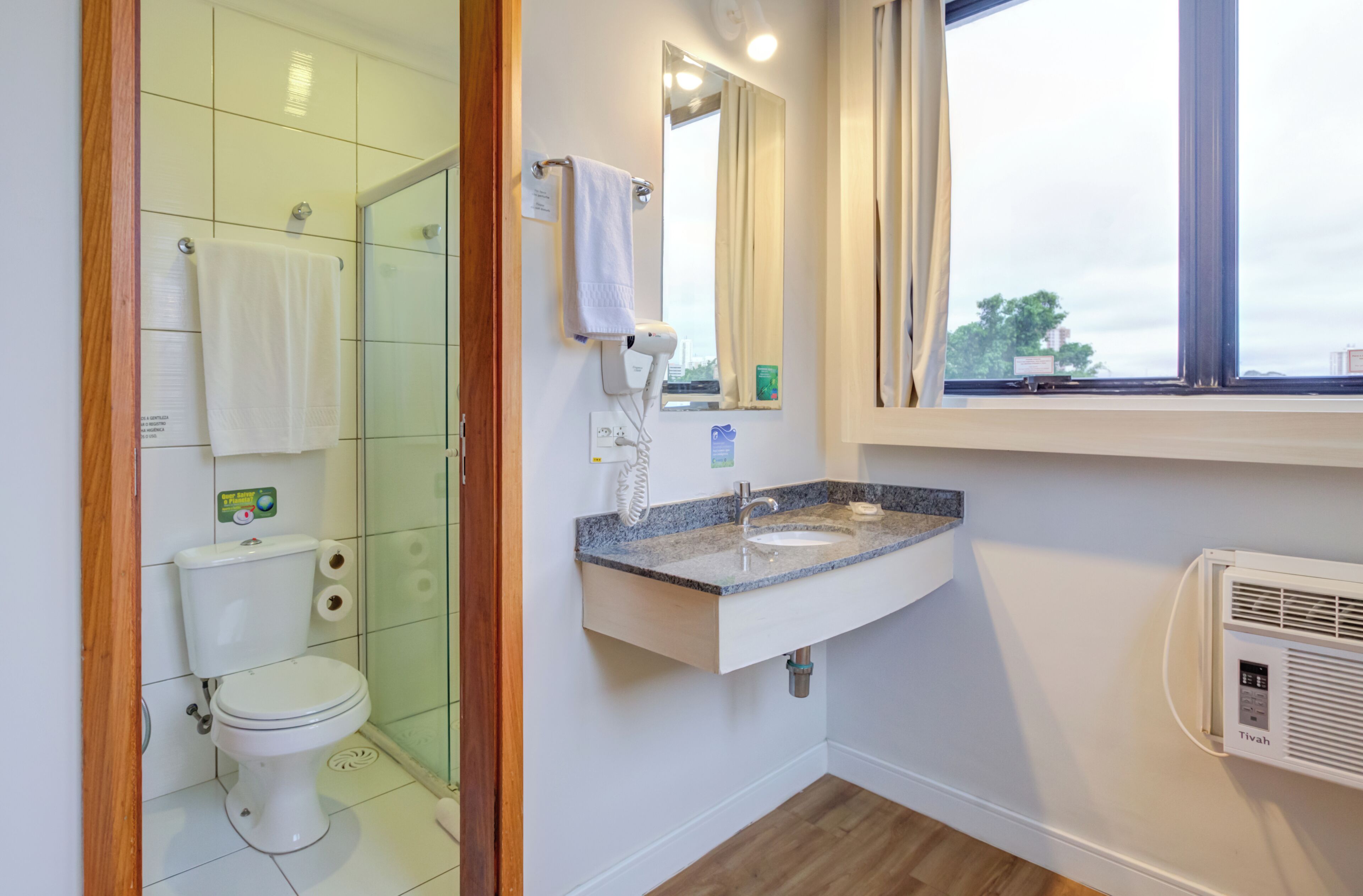 A bathroom with a toilet, a glass shower enclosure, a sink with a mirror, and a window.