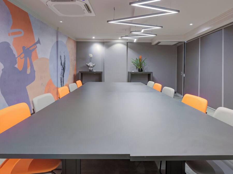 A conference room with a long table, orange and white chairs, a mural on the wall, and modern lighting fixtures.