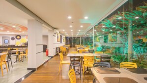 A spacious restaurant with wooden flooring, yellow and black chairs, and a long counter. - Transamerica Fit Villa Lobos (São Paulo)