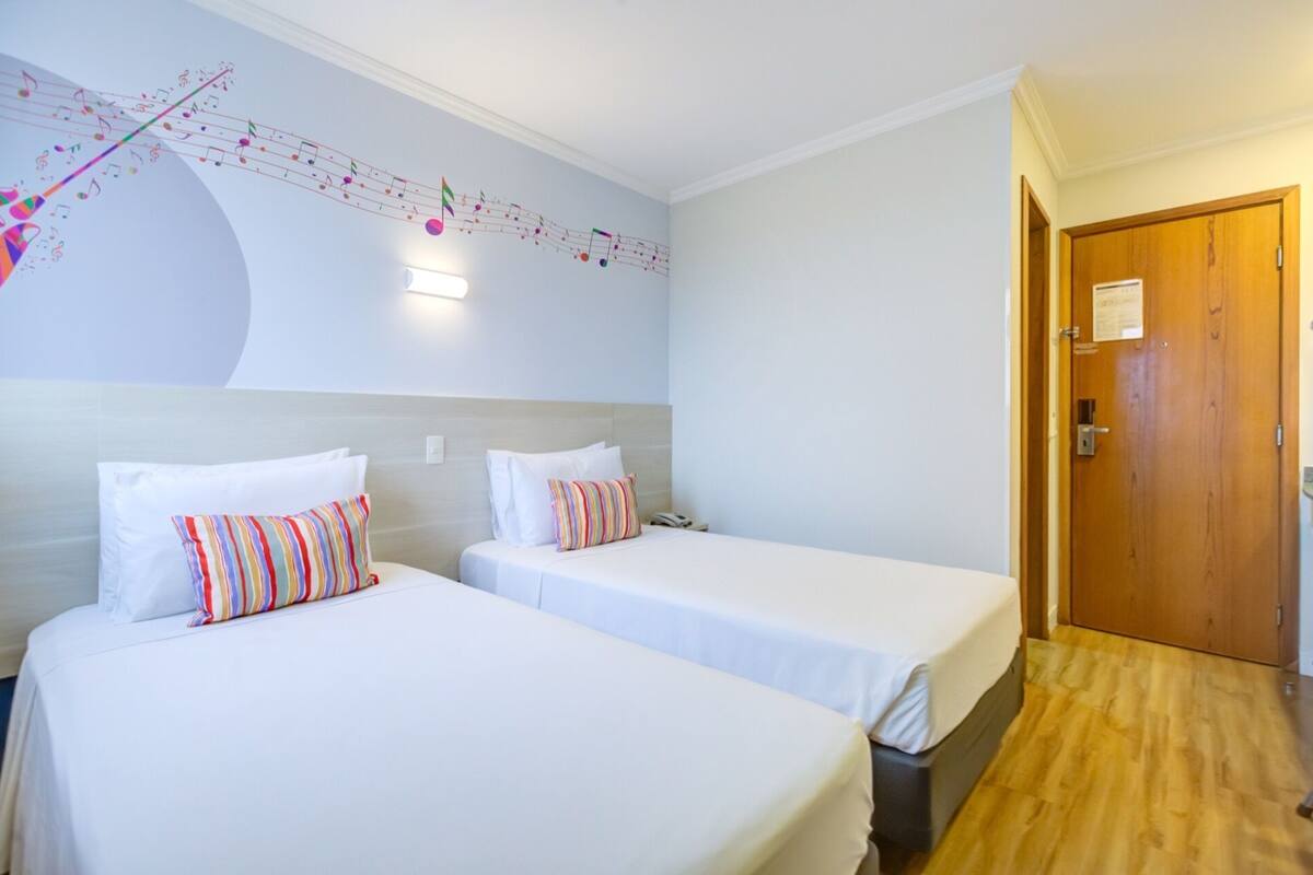 Ein Hotelzimmer mit zwei Einzelbetten, einer Holztür und einer Wand mit einer Noten-Grafik.