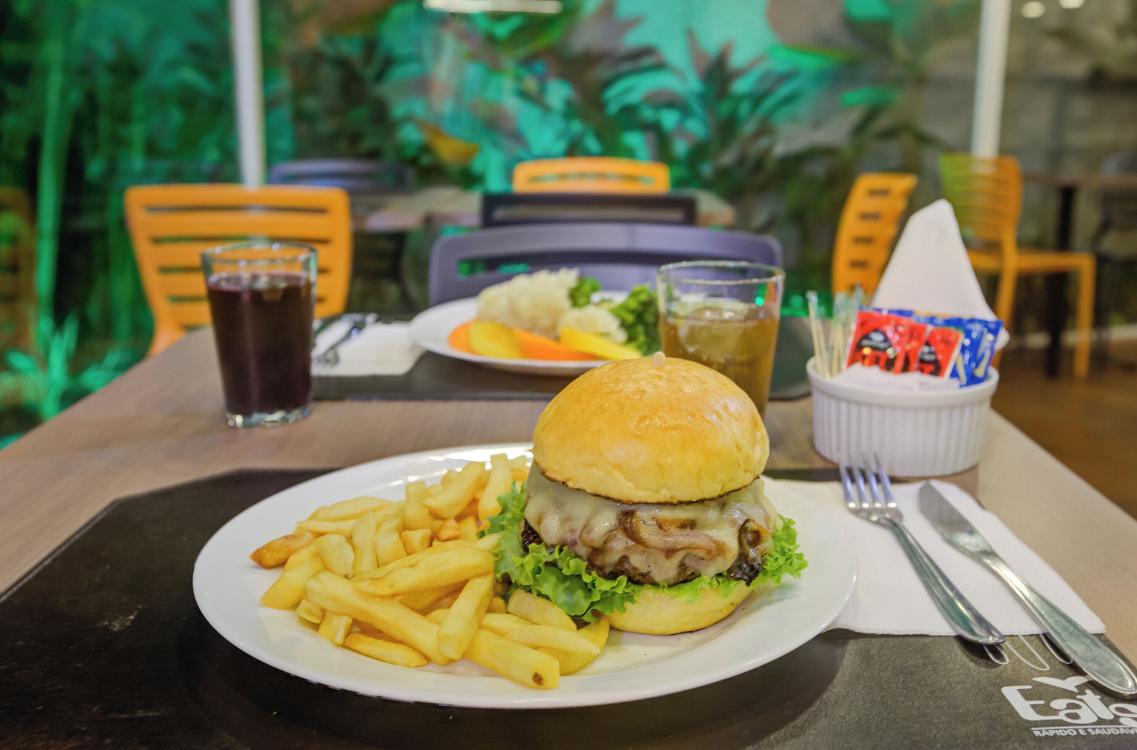A meal consisting of a burger and fries on a plate, with a drink and condiments in the background.