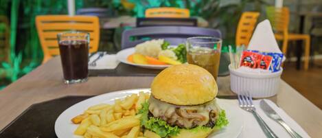 A meal consisting of a burger and fries on a plate, with a drink and condiments in the background.