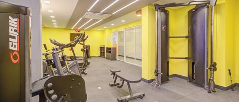 A gym with various exercise equipment, bright yellow walls, and a ceiling with linear lighting.