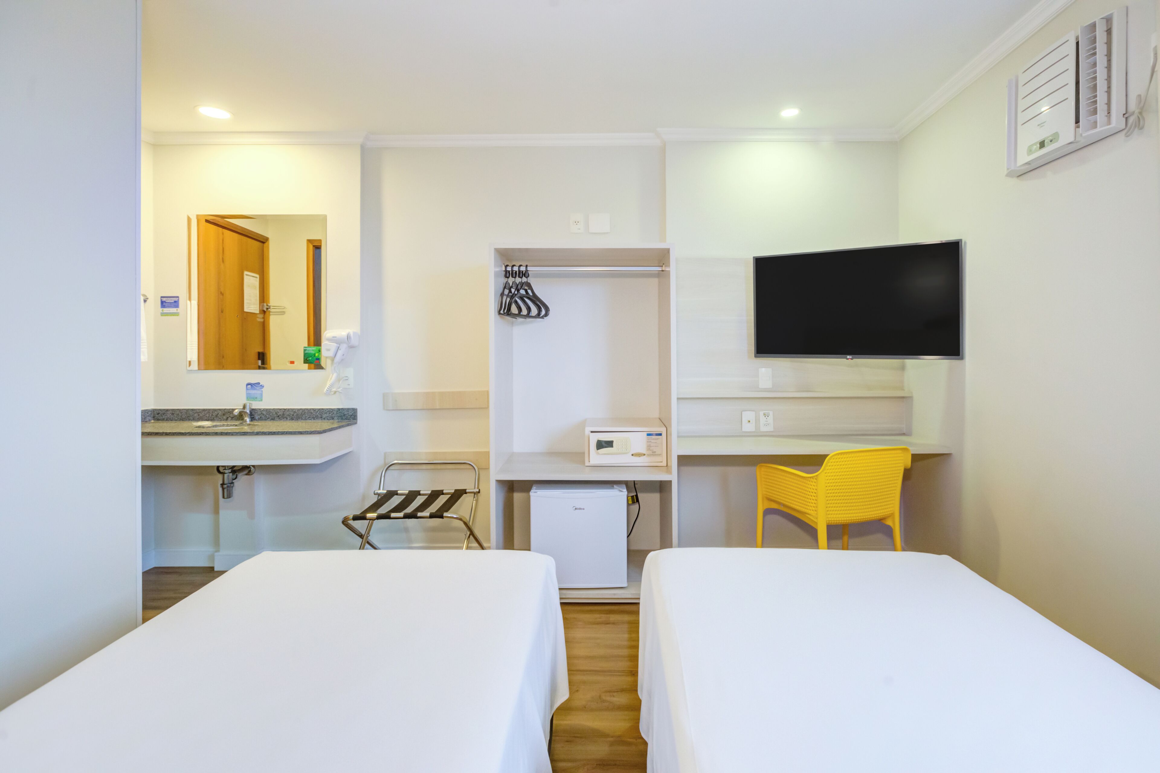 Hotelkamer met twee bedden, een kleine koelkast, een wastafel, een spiegel, een televisie en een stoel.