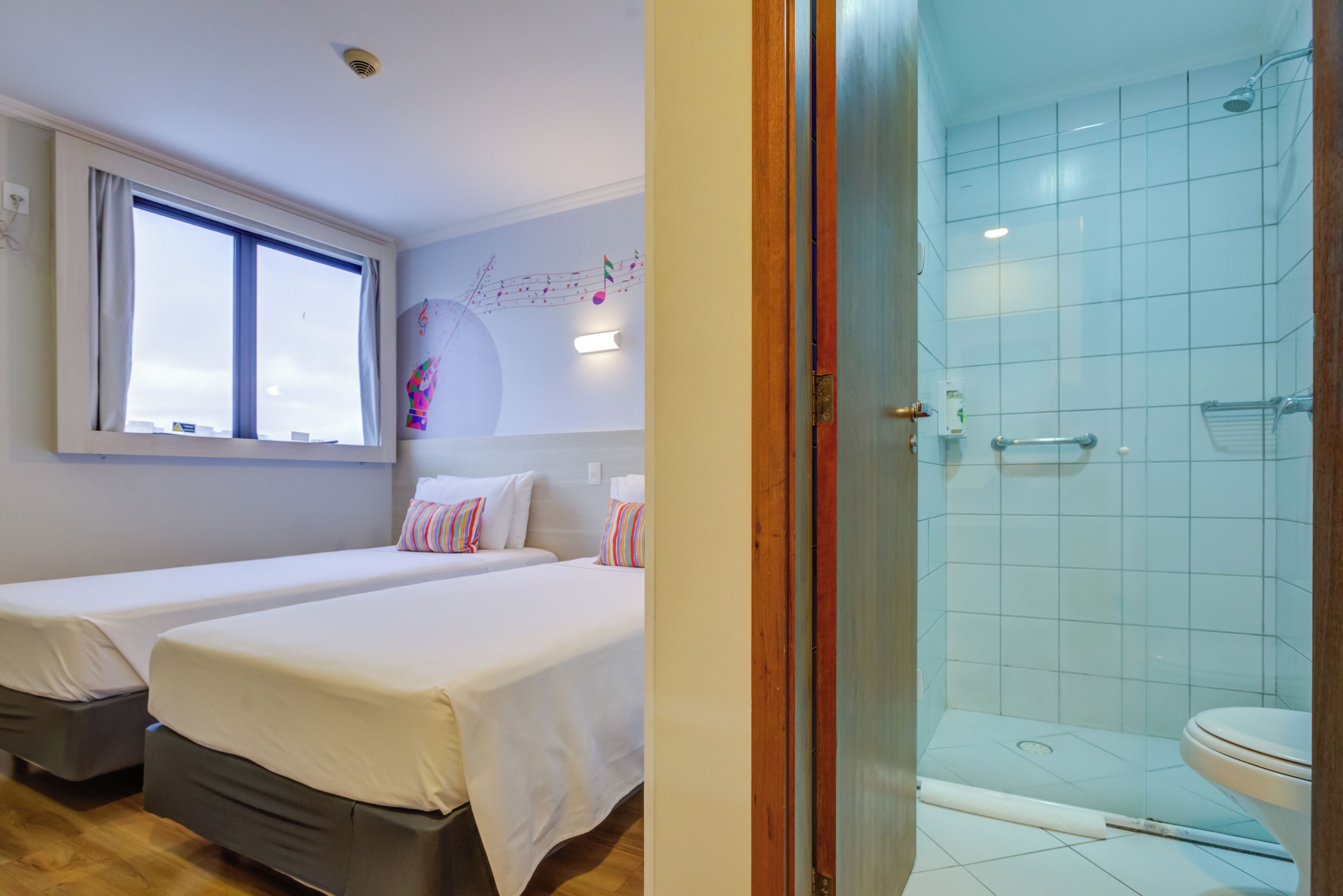 A hotel room with two beds, a window, a shower, and a toilet.