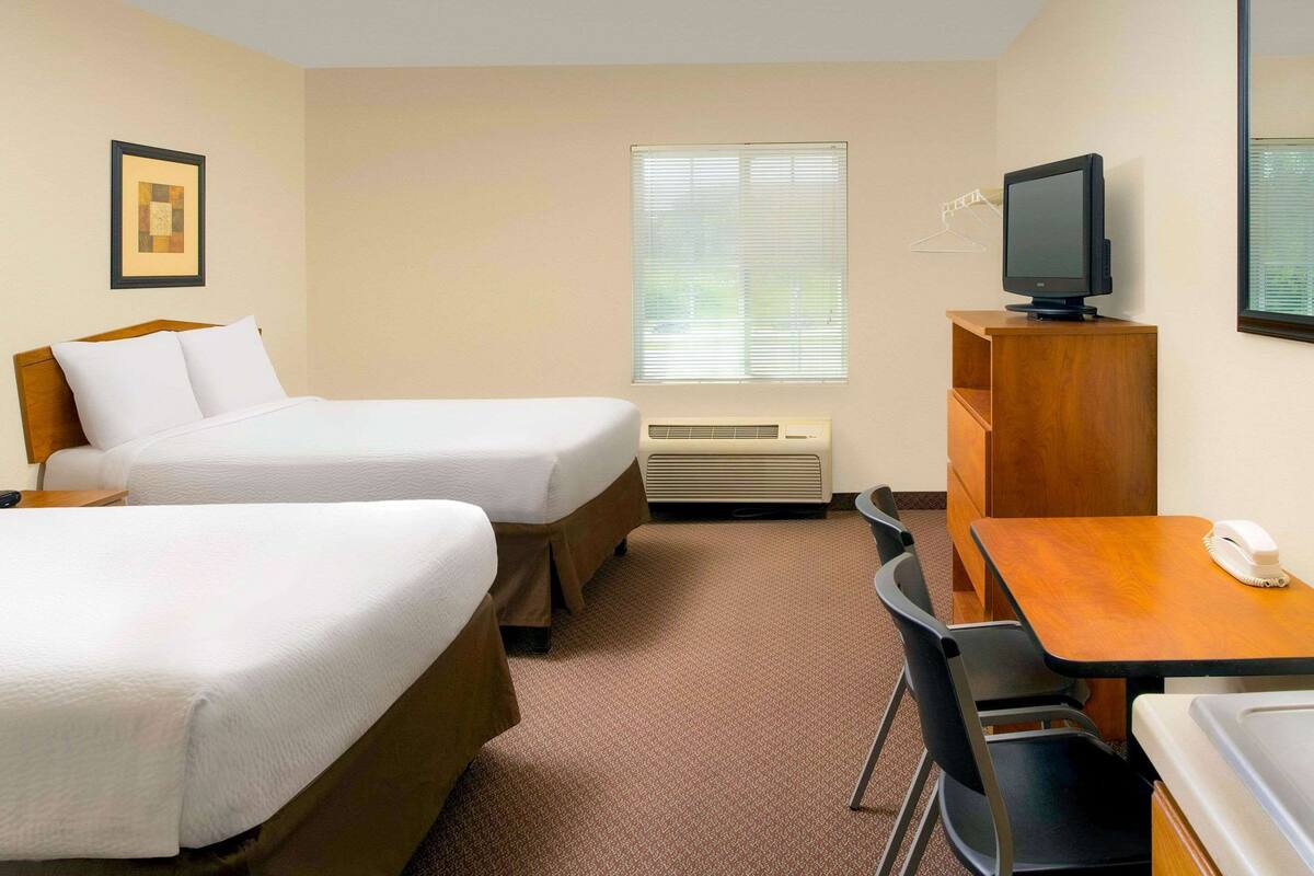 A hotel room with two beds, a desk, a chair, a television, and a window with blinds.