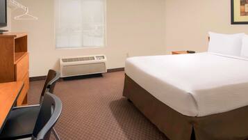 Een hotelkamer met een bed, een bureau, een stoel, een verwarming en een raam met jaloezieën.