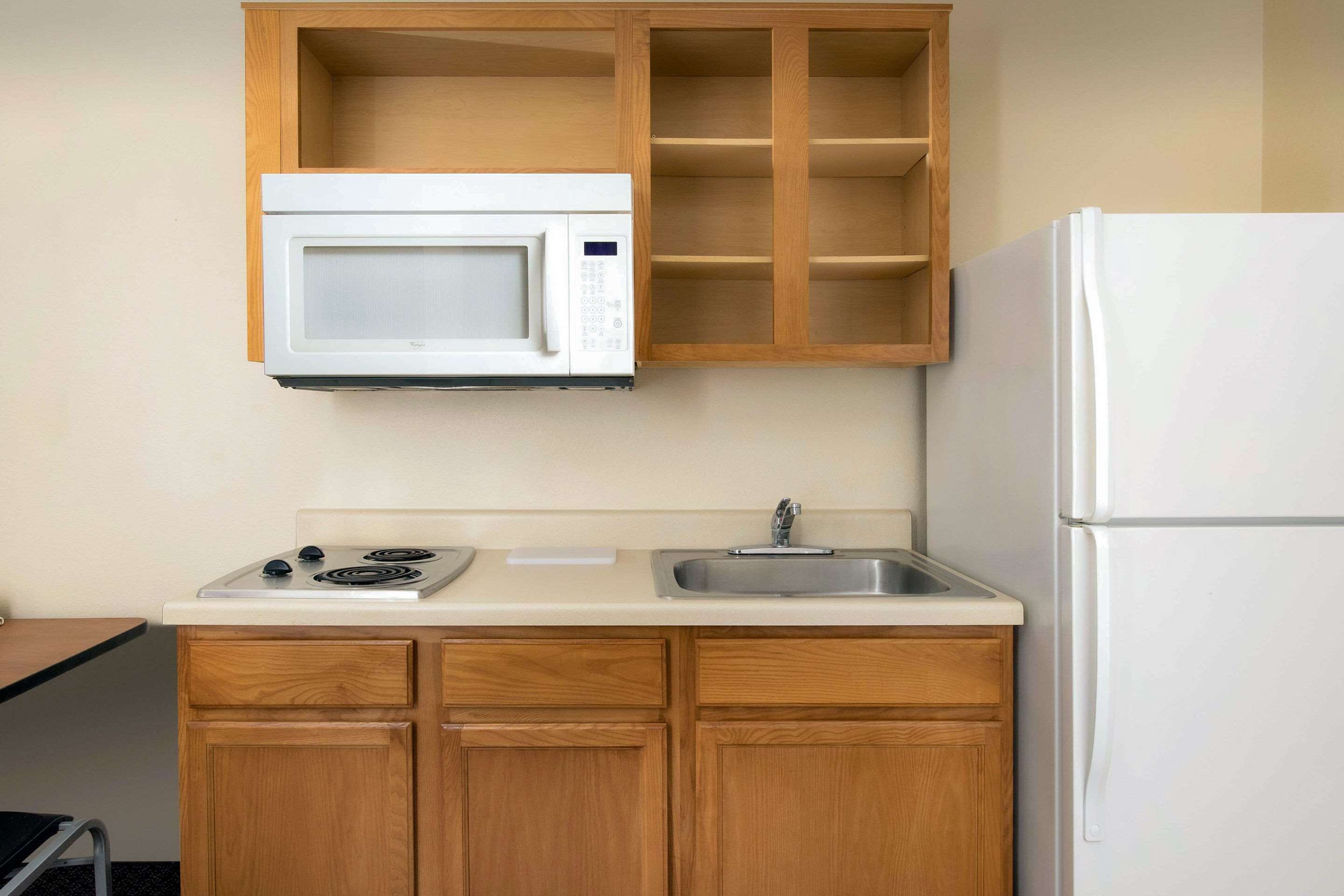 A compact kitchen with wooden cabinets, a white microwave, a stove, a sink, and a refrigerator.