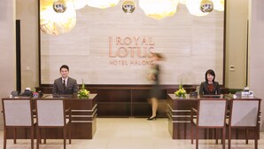 A reception desk at the Royal Lotus Hotel Halong with two staff members seated, a nameplate, and a cash register. - Royal Lotus Hotel Halong (Ha Long)