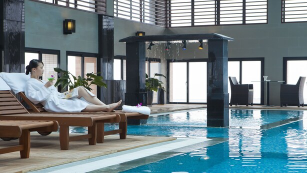 A pool area with wooden loungers, a water feature, and potted plants. - Royal Lotus Hotel Halong (Ha Long)