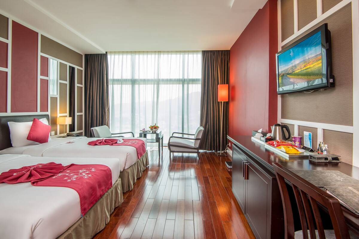 Une chambre d’hôtel avec deux lits, un bureau, une chaise, une télévision et une fenêtre avec des rideaux.