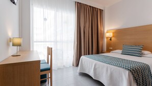 Una habitación de hotel con una cama, un escritorio, una silla, una lámpara y una ventana con cortinas.