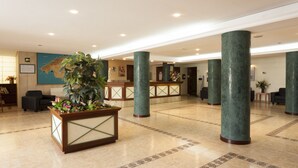 Un vestíbulo amplio con mostrador de recepción, grandes columnas verdes y una planta en maceta.