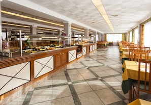A buffet area with a long counter, multiple food stations, and rows of tables and chairs. - Hotel Riutort (Palma de Mallorca)