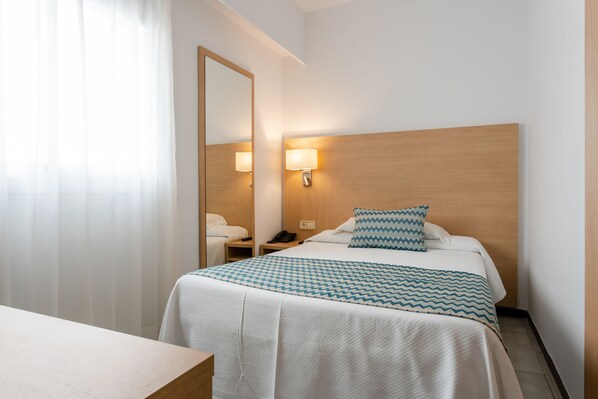 A hotel room with a bed, bedside lamps, a nightstand, a mirror, and a window with curtains.