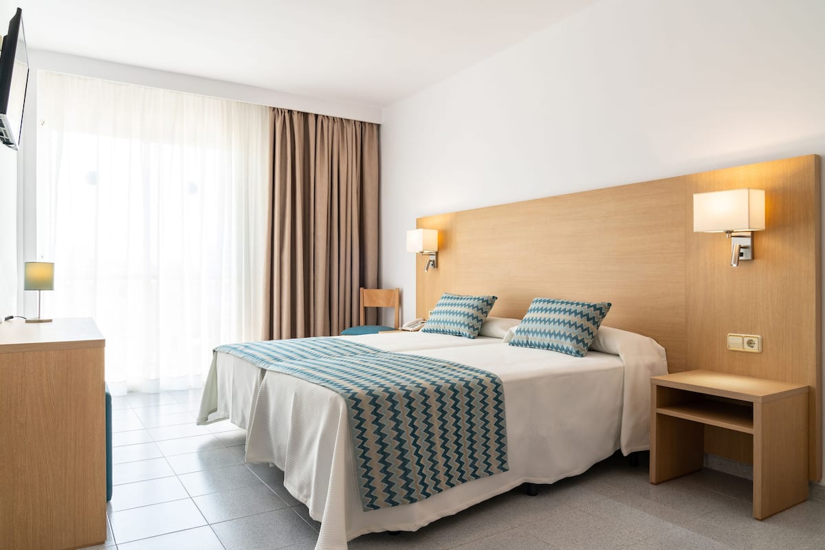 A hotel room with a large bed, bedside lamps, a wooden nightstand, and a desk with a lamp.