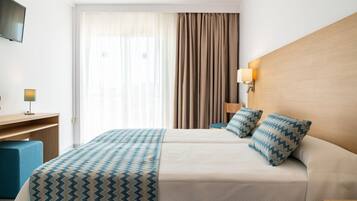 Una habitación de hotel con cama, escritorio, televisor y ventana con cortinas.
