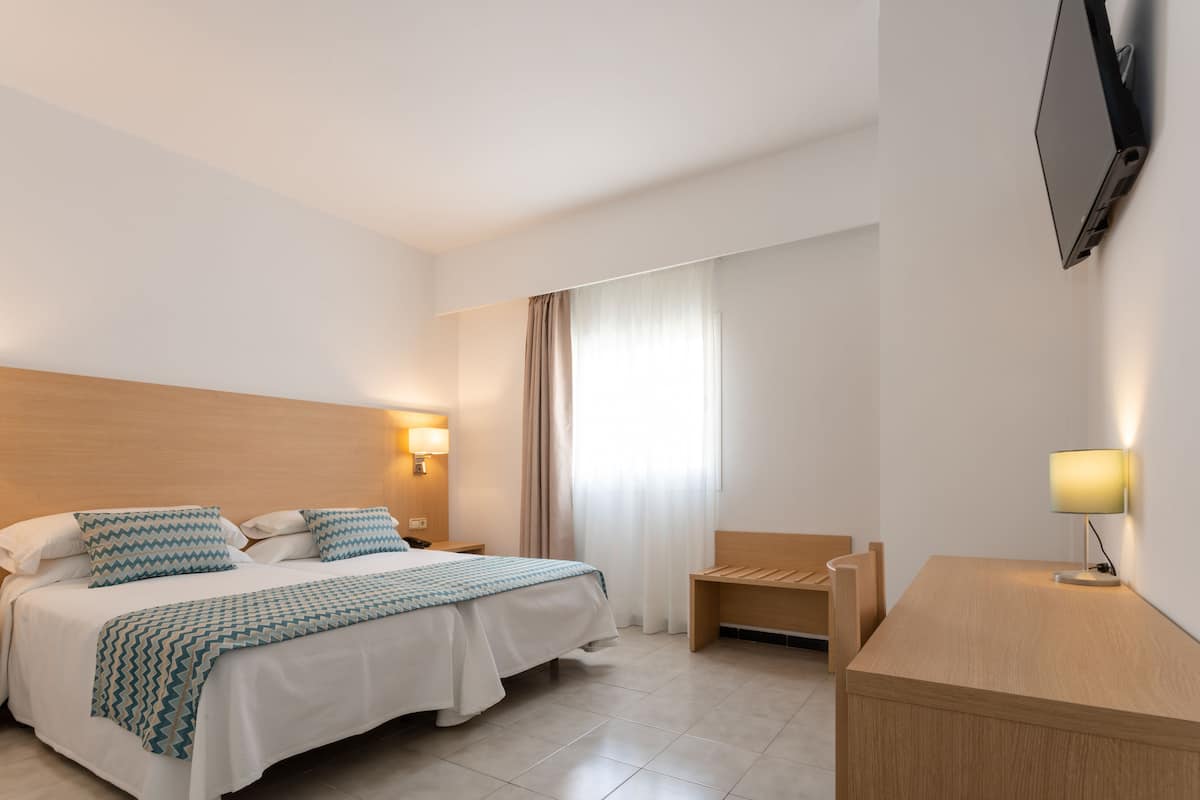 A hotel room with a bed, bedside lamps, a desk, and a TV mounted on the wall.