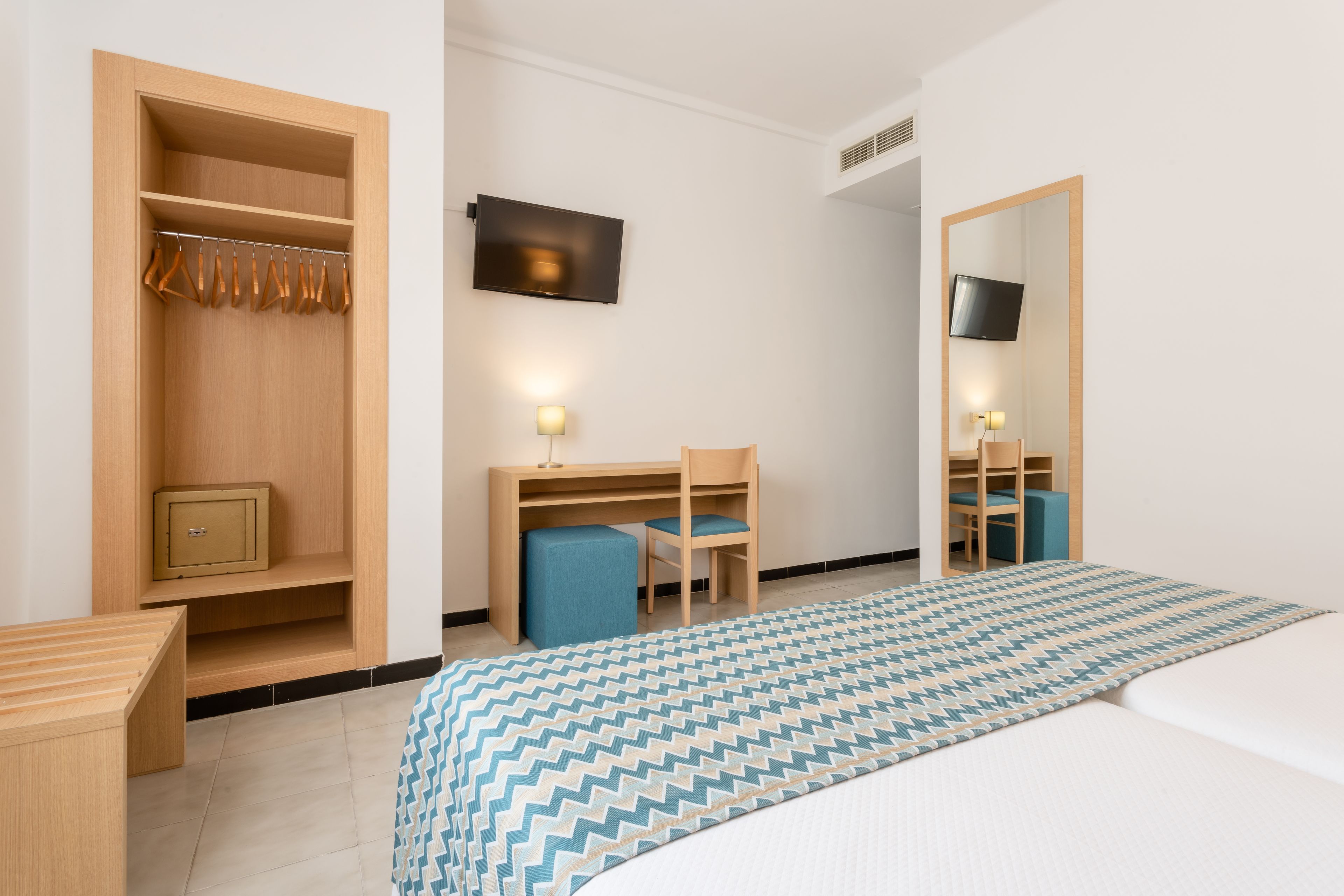 Habitación de hotel con cama, escritorio y silla, armario, televisor y espejo.