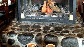 Lareira de pedra com fogo aceso, duas chávenas de café sobre uma mesa.