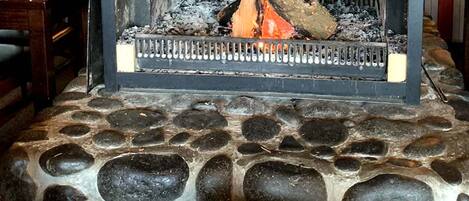 Una chimenea de piedra encendida, con dos tazas de café sobre una mesa.