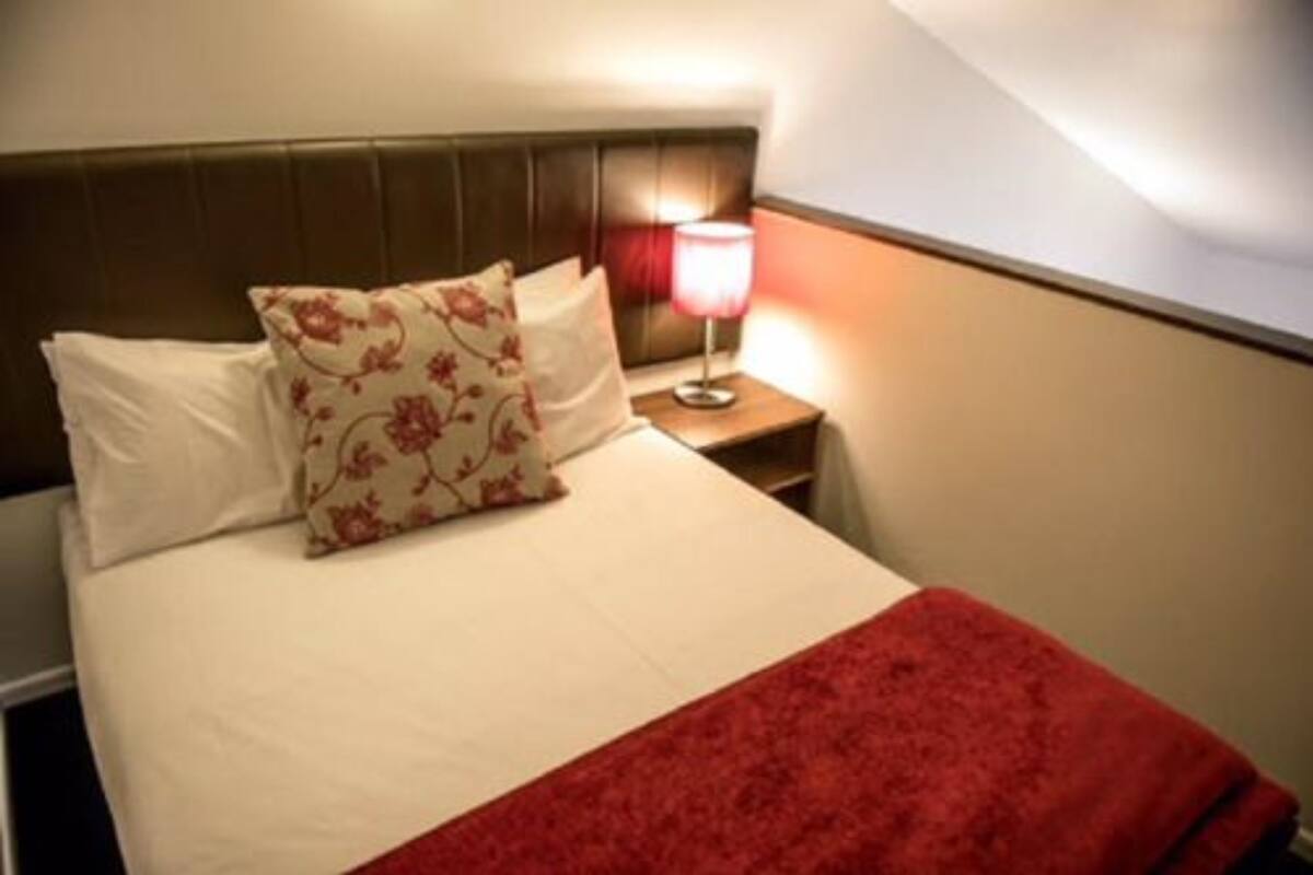 A neatly made bed with white and red bedding, a floral pillow, and a red throw blanket.