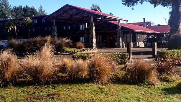 Eine Lodge mit rotem Dach und Steinpfeilern, umgeben von einem angelegten Garten mit hohem Gras.