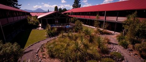 A building with a red roof and a pool surrounded by a garden with various plants.