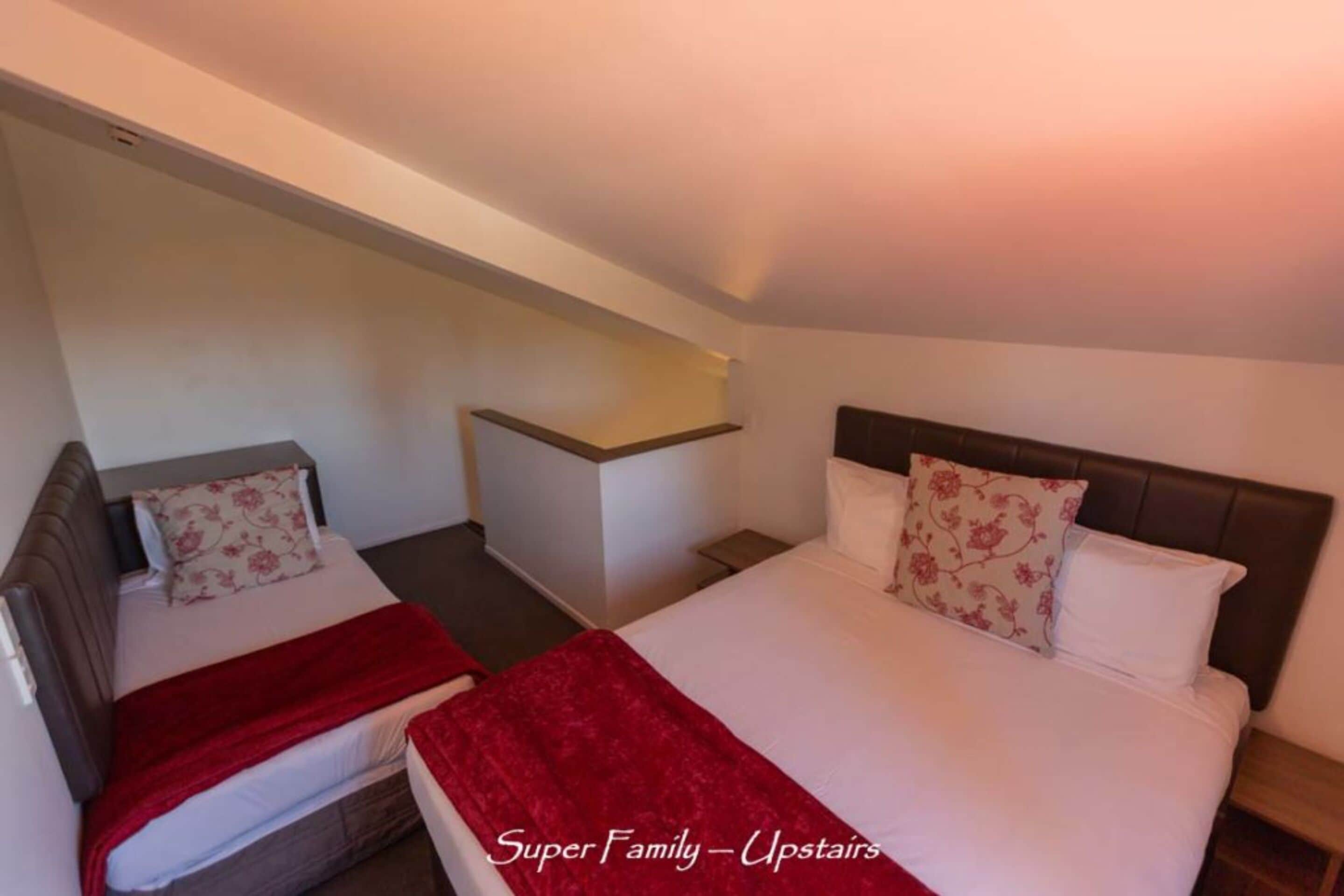 Habitación de hotel con dos camas, una con una manta roja y cabecera con un almohadón floral.