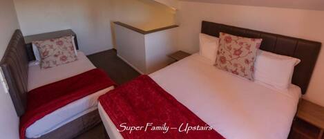Habitación de hotel con dos camas, una con una manta roja y cabecera con un almohadón floral.