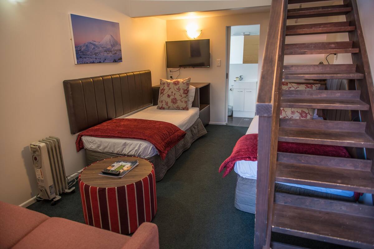 A hotel room with a bed, a TV, a wooden staircase, and a view of a mountain.