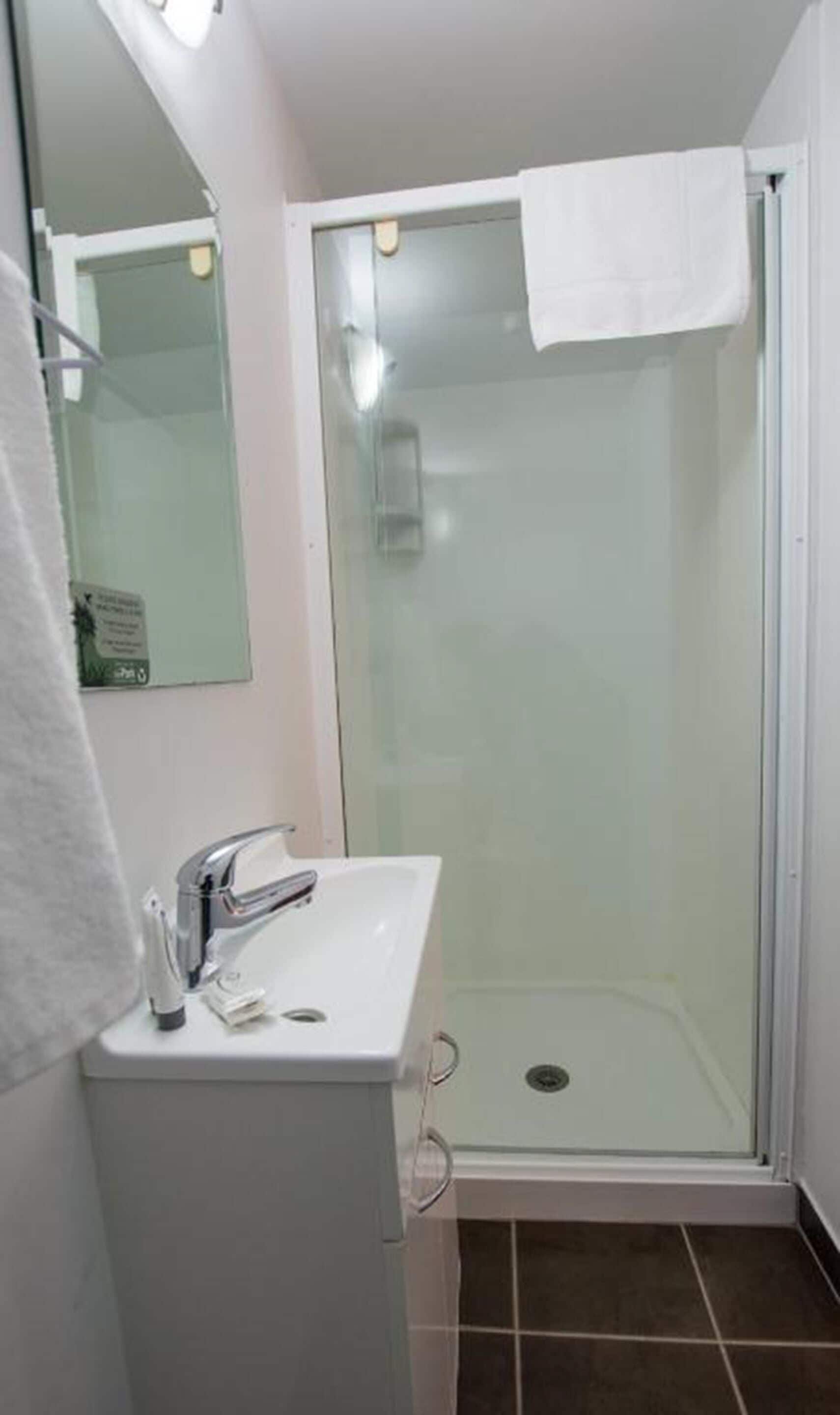 Un baño con ducha de vidrio, un lavabo blanco y un espejo.