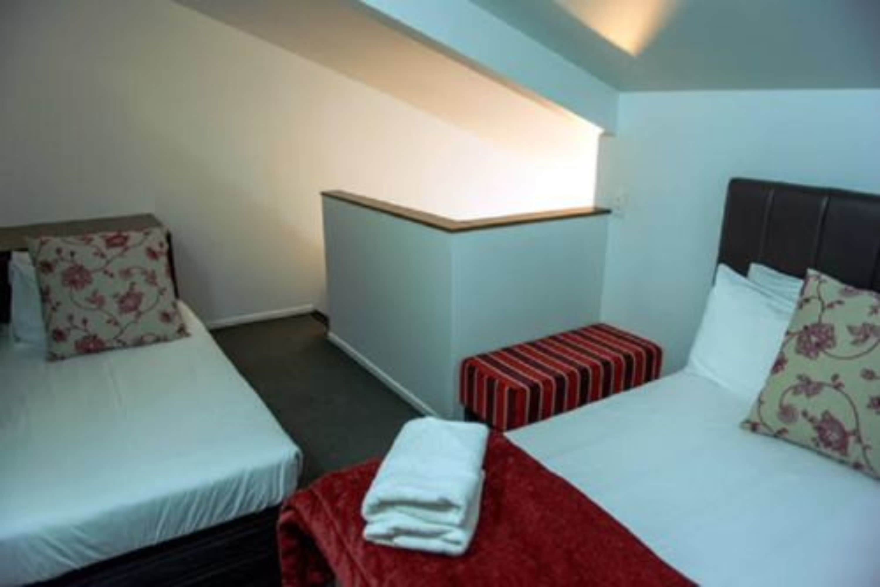 A hotel room with two beds, a small table, and a bench.