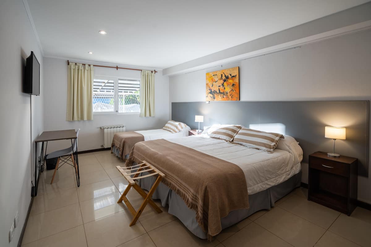 A bedroom with two beds, a desk, a chair, a lamp, and a painting on the wall.