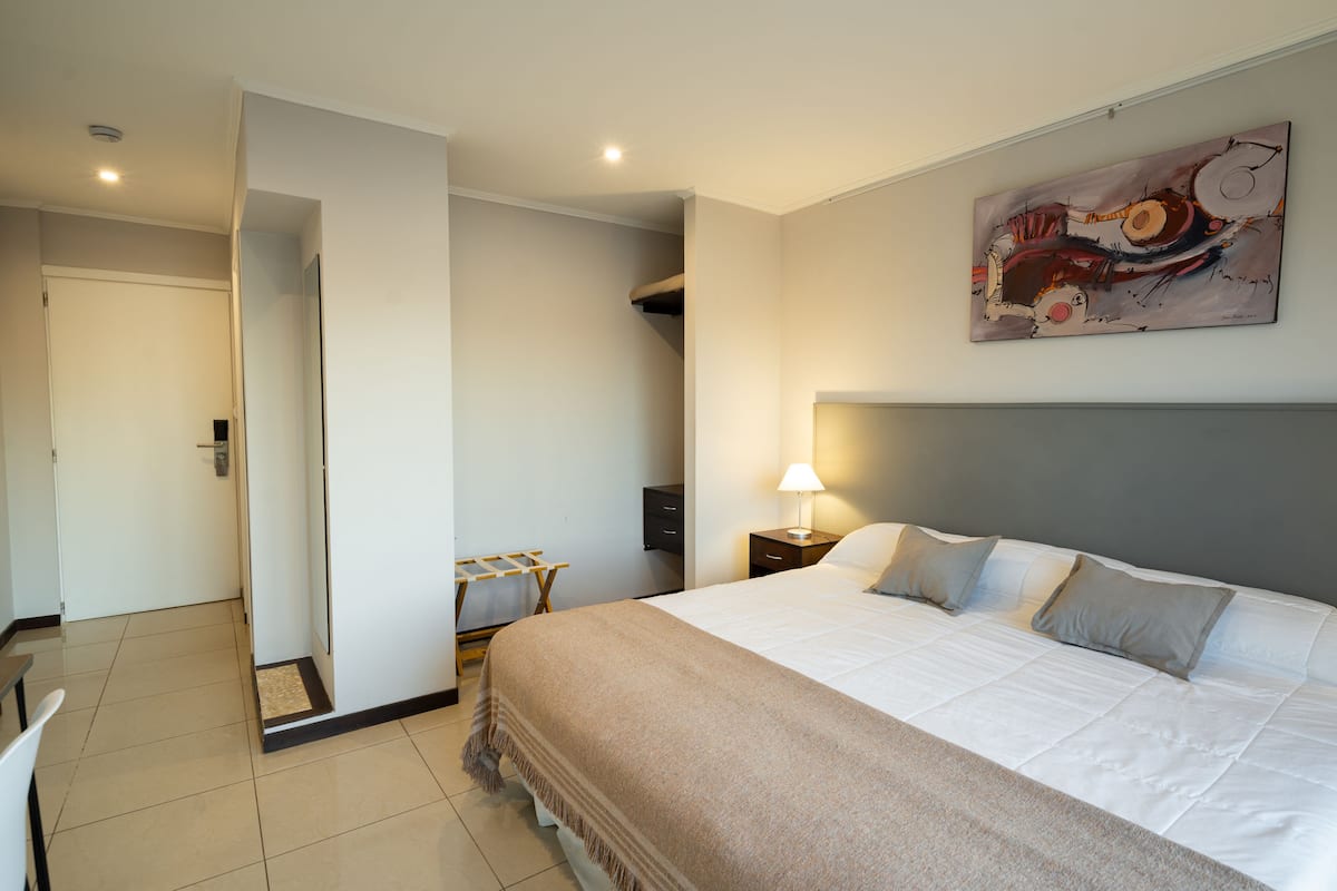A hotel room with a large bed, a nightstand with a lamp, a painting on the wall, and a staircase leading to another room.