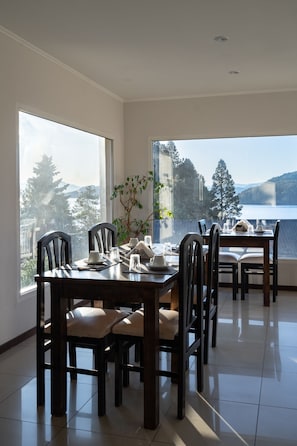 A dining area with a view of a lake and mountains, wooden furniture, and a potted plant. - NBH Lacus Boutique Hotel (San Carlos de Bariloche)