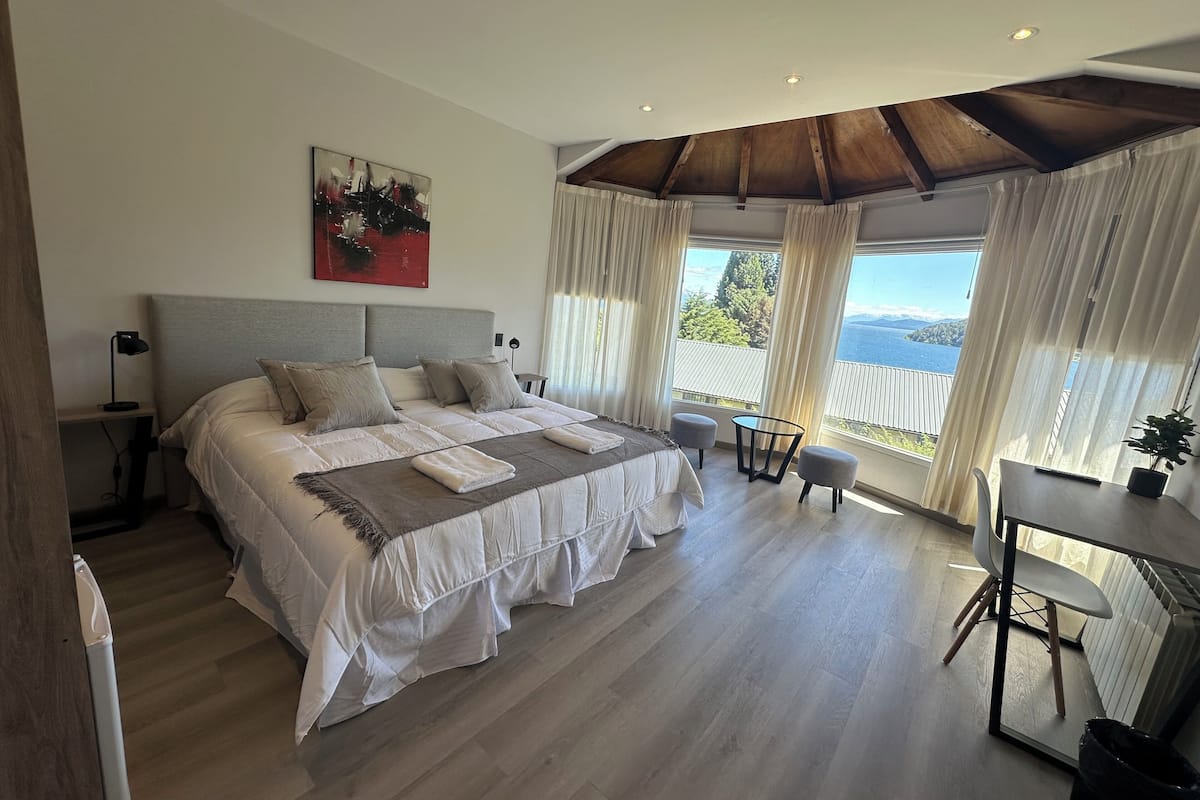 A bedroom with a large bed, a desk, and a view of the sea.