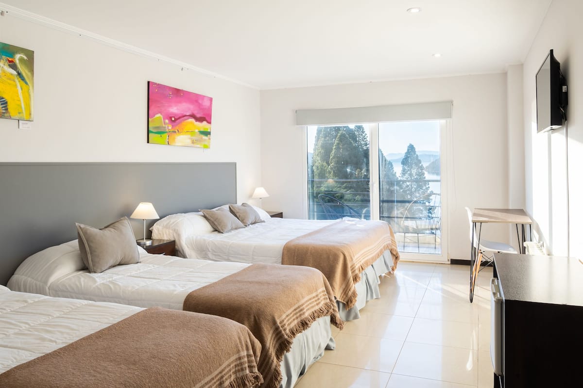 A hotel room with two beds, a desk, and a large window with a view.
