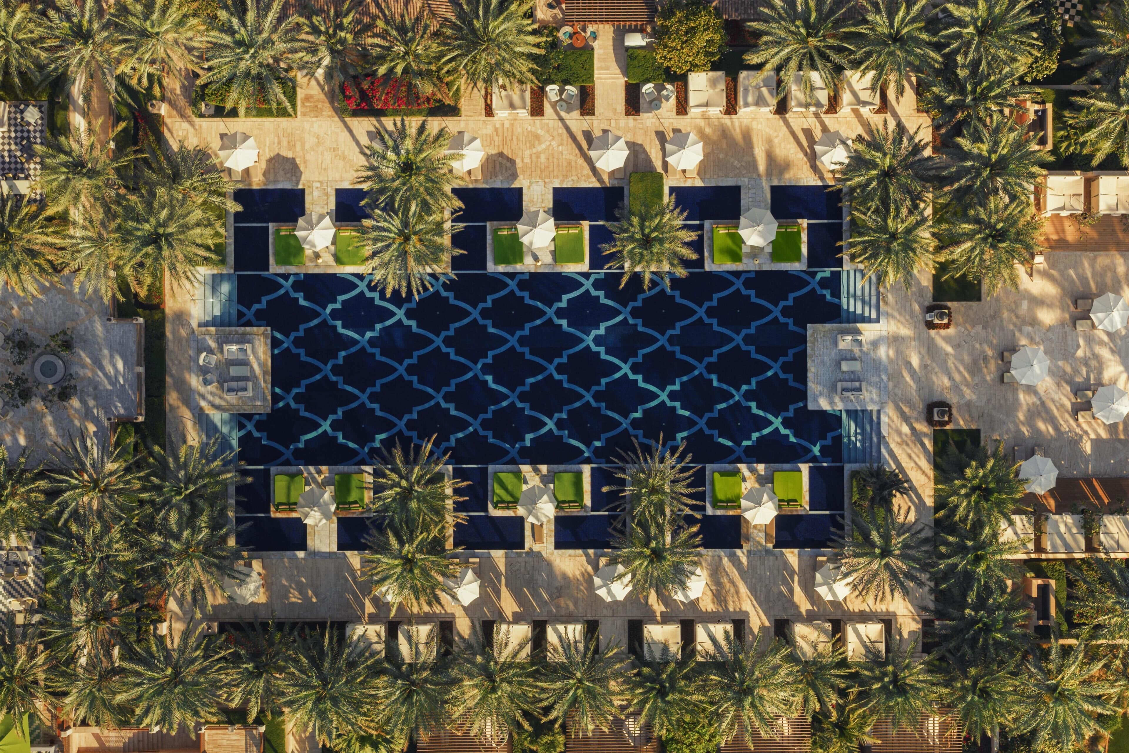 Vue aérienne d’un hôtel doté d’une piscine centrale, entouré de palmiers et agrémenté d’espaces de détente en plein air.