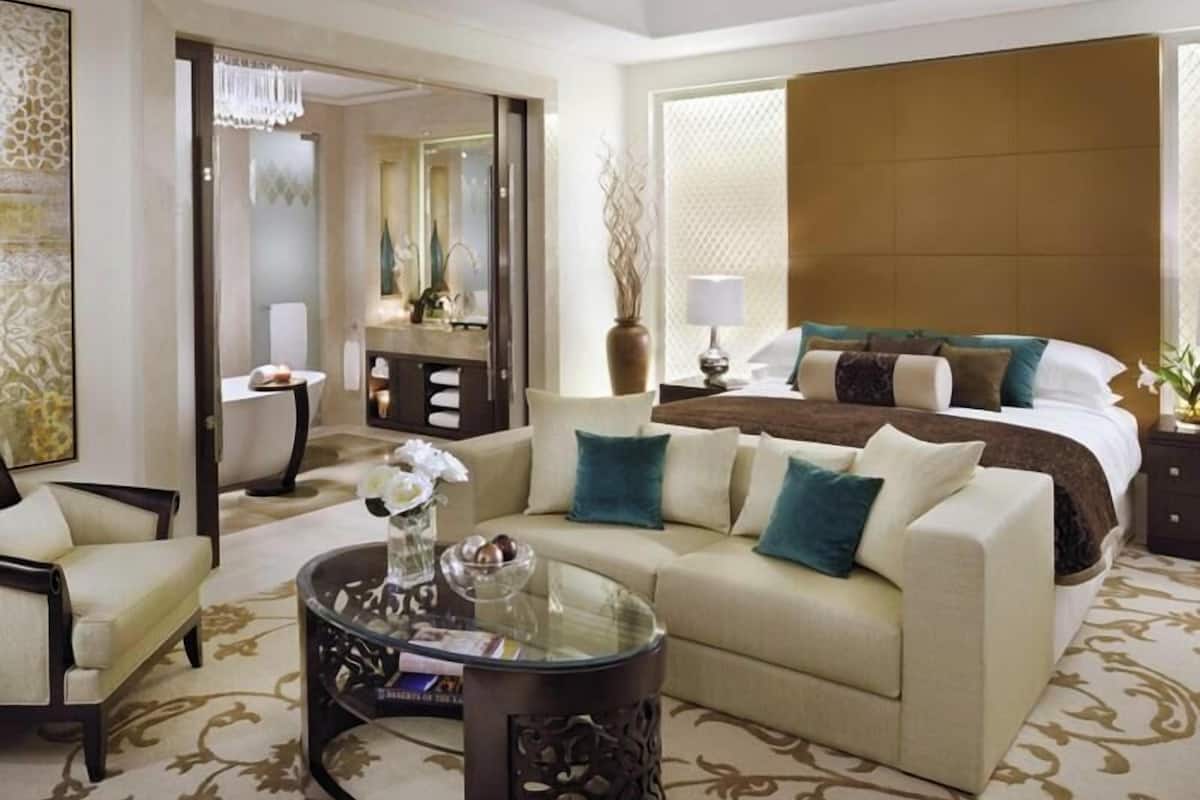A hotel room with a bed, a sofa, a glass coffee table, a dresser, and a mirror.