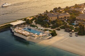 An aerial view of a resort with a swimming pool, beach, and villas.