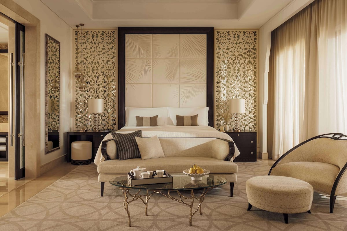 A modern bedroom with a large bed, a sofa, a glass coffee table, and a chair.