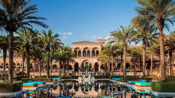 A luxurious resort with a central pool, palm trees, and a grand building with arches. - One&Only The Palm (Dubai)