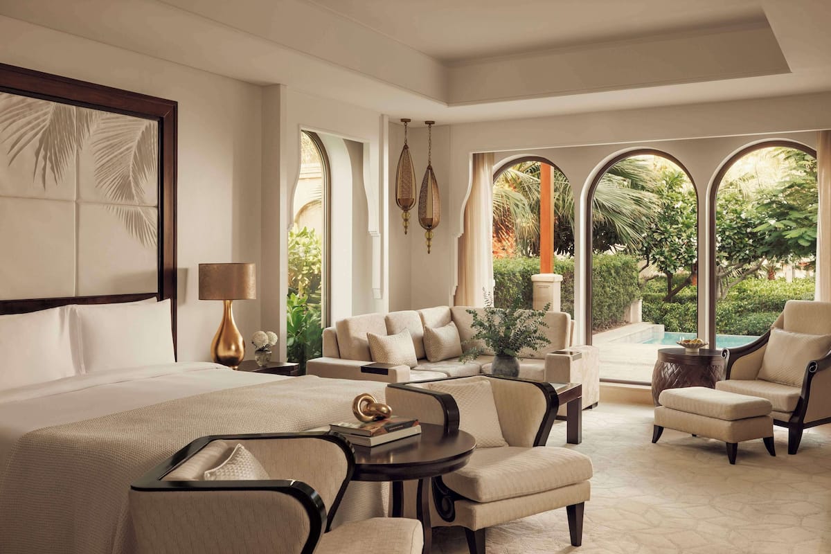 A spacious bedroom with a large bed, multiple seating areas, and a view of a swimming pool.