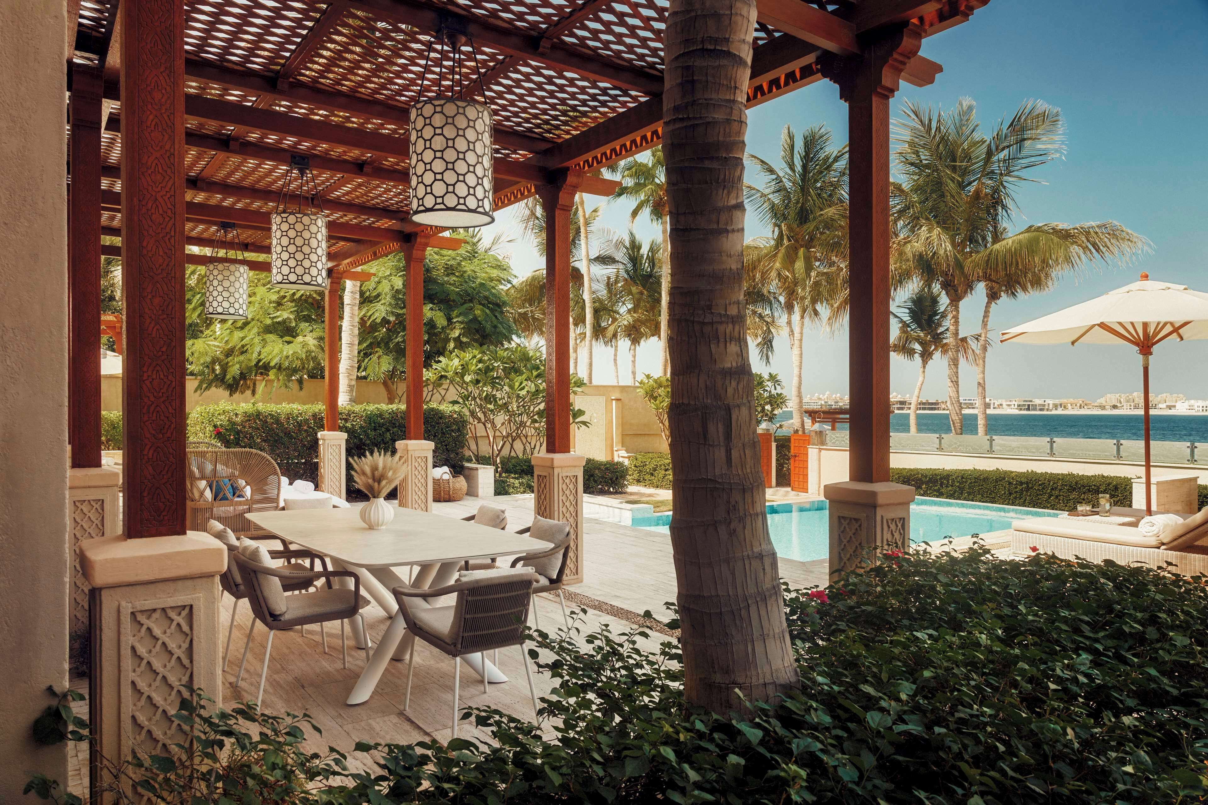 A covered outdoor area with a pool, palm trees, and a view of the sea.